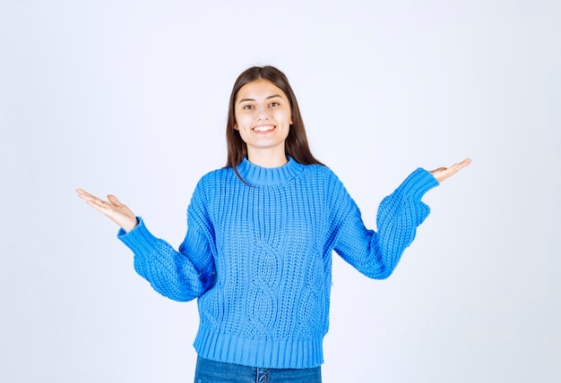 Portret van een tienermeisje in een blauwe trui die staat en vrolijk glimlacht.