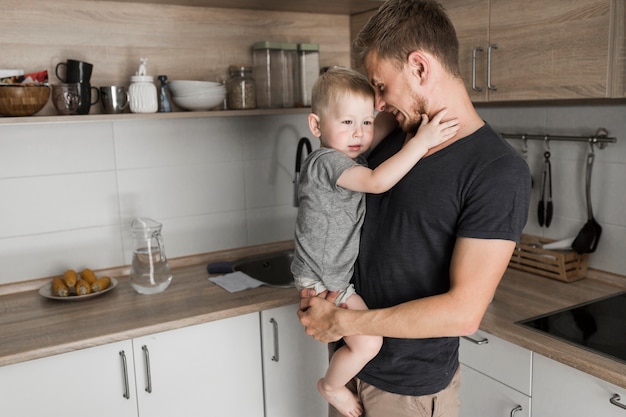 Portret van een vader die zijn leuke zoon vervoert die zich in de keuken bevindt