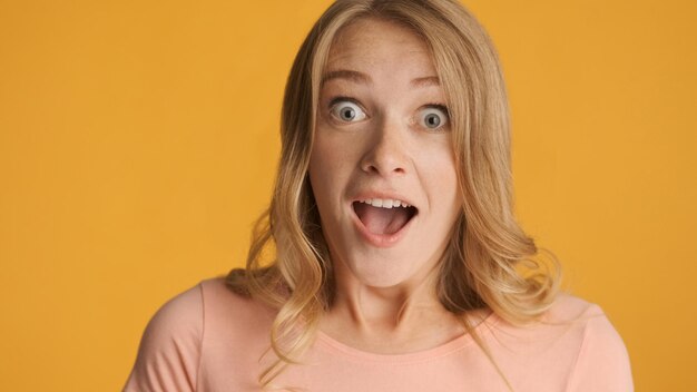 Portret van een verbaasd blond meisje houdt de mond verrassend open en kijkt in de camera geïsoleerd op een kleurrijke achtergrond Wow-expressie