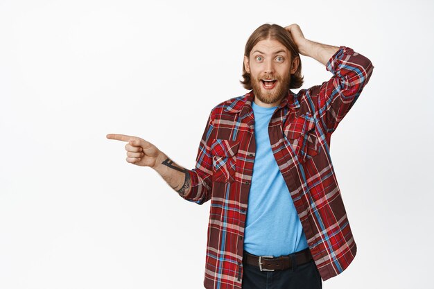 Portret van een verbaasde blonde man hapt naar adem, wijst met de vinger naar links en houdt de hand op het hoofd, verbaasd over iets indrukwekkends, banner, witte achtergrond.