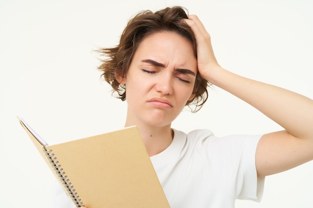 Portret van een verbaasde jonge vrouw die het beu is om huiswerk te maken met een planner met een ingewikkeld gezicht