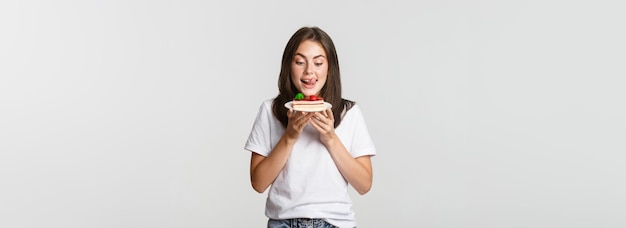 Portret van een verleid mooi meisje dat lippen likt terwijl ze naar cake kijkt