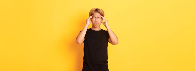 Portret van een verontruste aziatische mannelijke student met hoofdpijn die grijnzend van pijn en het aanraken van het hoofd lijdt