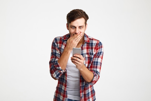 Portret van een verrast casual man kijken naar mobiele telefoon