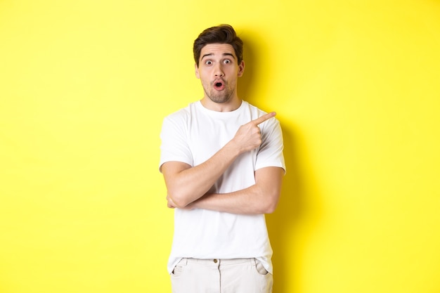 Portret van een verraste knappe man die met de vinger naar rechts hijst en verbaasd staat over een gele achtergrond