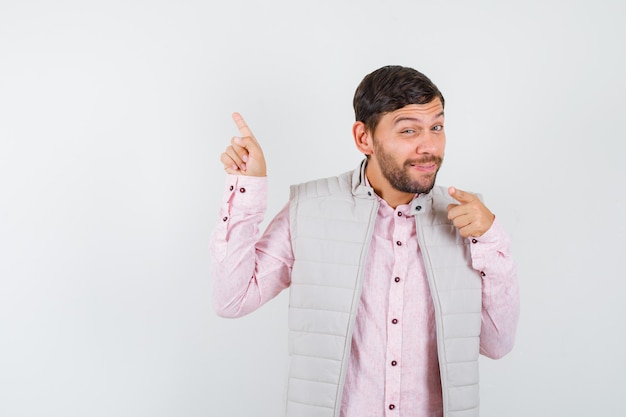 Portret van een volwassen man die naar de linkerbovenhoek wijst in shirt, mouwloos jasje en er vrolijk vooraanzicht uitziet