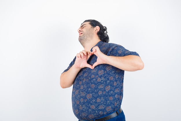 Portret van een volwassen man hart gebaar in shirt tonen en op zoek weemoedig vooraanzicht