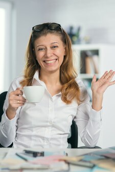 Portret van een volwassen zakenvrouw in een bril op kantoor haar werkplek met een kopje koffie of thee