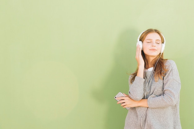 Portret van een vrij jonge vrouw het luisteren muziek op hoofdtelefoon door mobiele telefoon tegen munt groene achtergrond