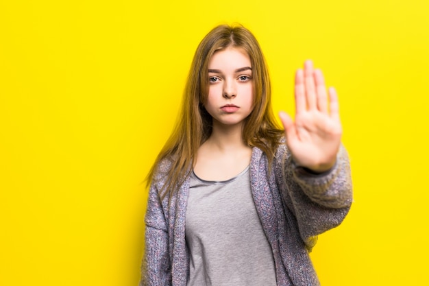 Portret van een vrij lachende vrouw geïsoleerd op een gele muur. Meisje dat stopgebaar met hand maakt