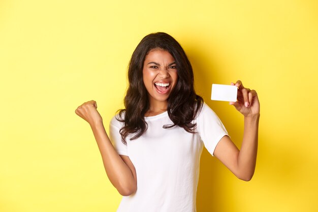 Portret van een vrolijk afro-amerikaans vrouwelijk model dat een creditcard toont en blij schreeuwt van vreugde