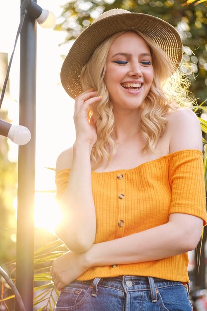 Portret van een vrolijk blond meisje met een hoed die vrolijk lacht terwijl ze op straat in de stad staat