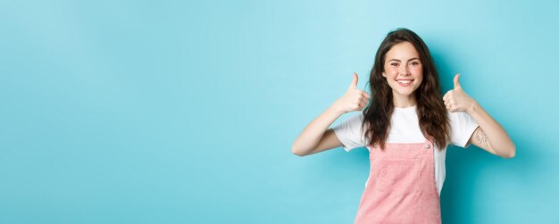 Portret van een vrolijk brunette meisje dat duimen laat zien en glimlacht en goed werk goedkeurt en aanbeveelt