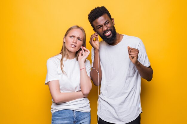 Portret van een vrolijk paar dat zingt tijdens het gebruik van smartphone en oortelefoons samen geïsoleerd over gele muur