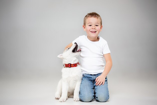 Portret van een vrolijke kleine jongen die plezier heeft met Siberische husky puppy op de vloer in de studio