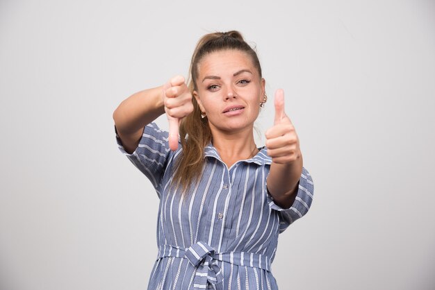 Portret van een vrouw die duimen op en neer geeft op grijze muur.