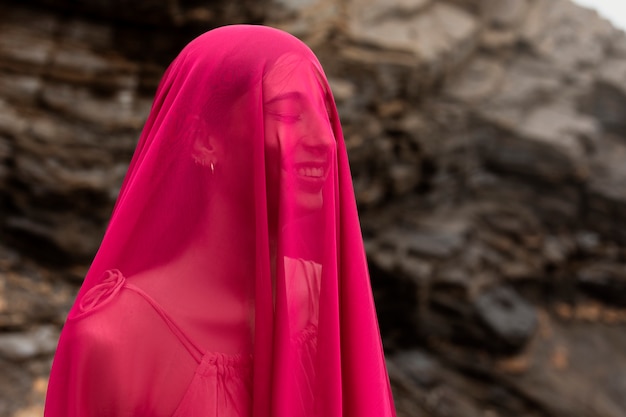 Portret van een vrouw die haar gezicht bedekt met een sluier op het strand