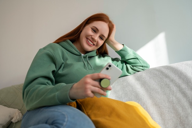 Portret van een vrouw die haar smartphone thuis op de bank gebruikt door haar uit de pop-socket te houden