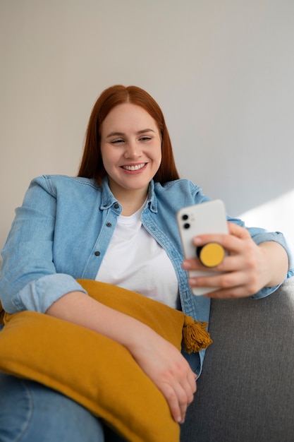 Portret van een vrouw die haar smartphone thuis op de bank gebruikt door haar uit de pop-socket te houden