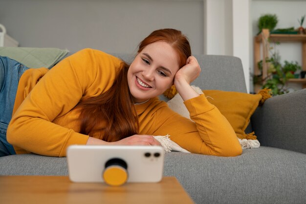 Portret van een vrouw die haar smartphone thuis op de bank gebruikt door haar uit de pop-socket te houden