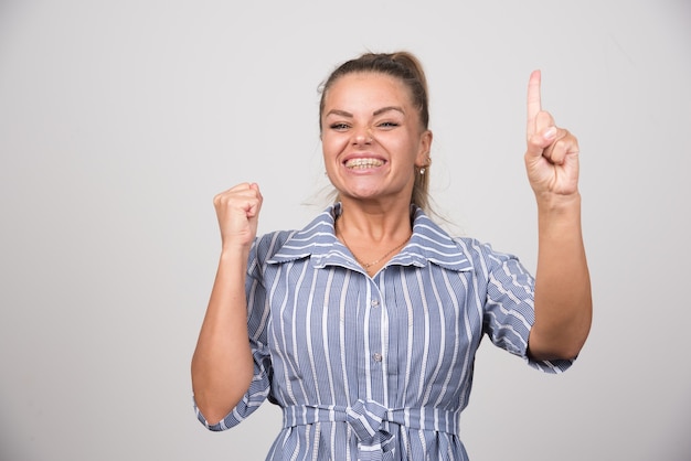 Portret van een vrouw die haar vinger op een grijze muur toont.