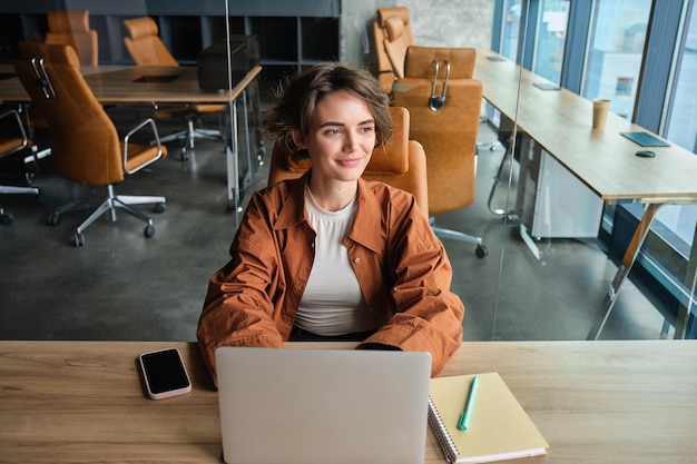 Gratis foto portret van een vrouw die op kantoor werkt en aan tafel zit met een laptopmeisje die programmeur codeert in coworking