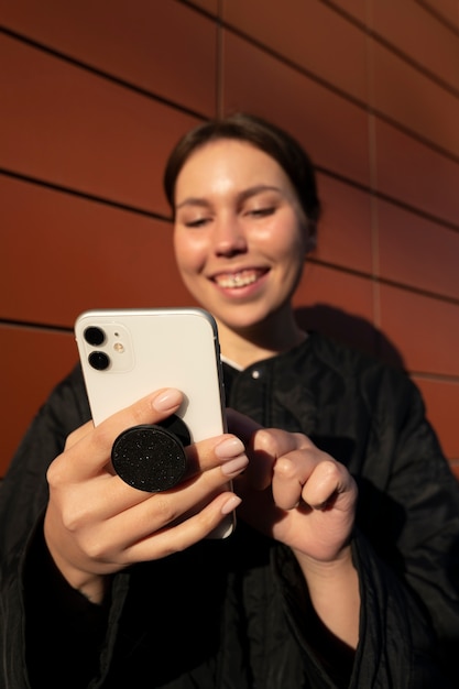 Portret van een vrouw die smartphone met pop-socket buitenshuis gebruikt