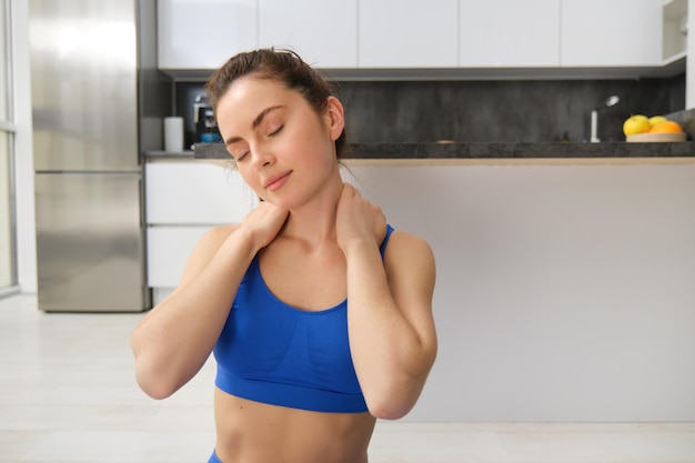 Portret van een vrouw die thuis traint, oefeningen doet, haar nek strekt, zich opwarmt voor fitness