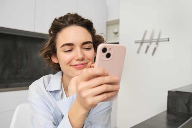 Gratis foto portret van een vrouw die thuis zit en haar mobiele telefoon controleert en naar een smartphone kijkt met blij