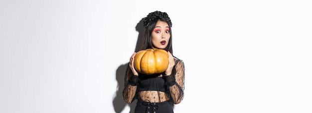 Gratis foto portret van een vrouw die zware pompoen optilt en zich klaarmaakt voor halloween met een heksenkostuum dat staat