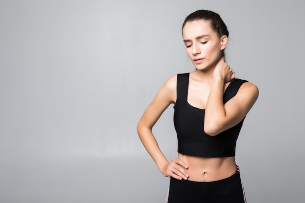 Portret van een vrouw in een fitness outfit ervaren nek-, schouder- en rugpijn geïsoleerd op een witte muur