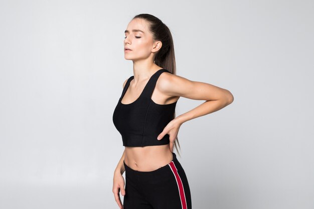Portret van een vrouw in een fitness outfit ervaren nek-, schouder- en rugpijn geïsoleerd op een witte muur