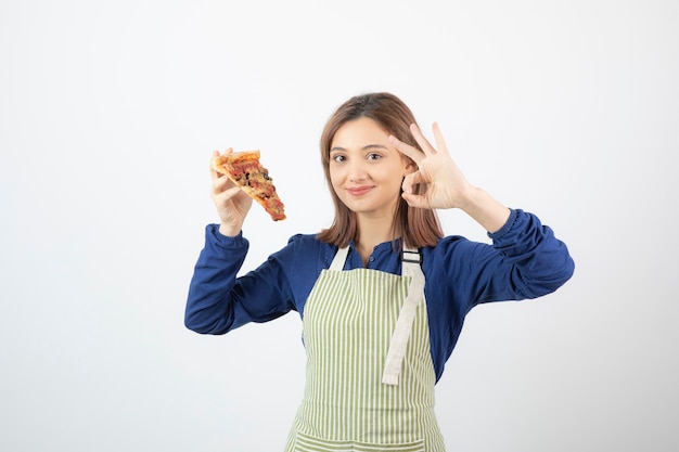 Portret van een vrouw in een schort die een stuk pizza op wit toont