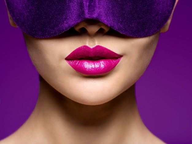 Portret van een vrouw met violet theatermasker op gezicht en paarse lippen
