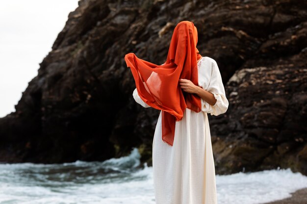 Portret van een vrouw op het strand die haar gezicht bedekt met een sluier