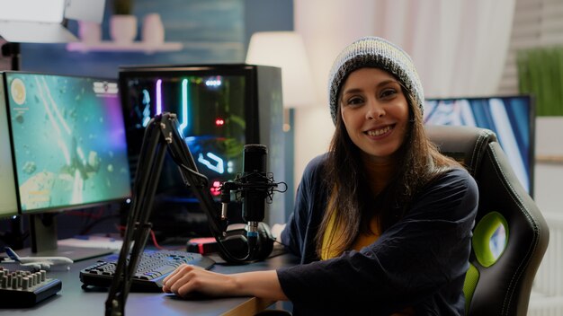 Portret van een vrouw-streamer die naar de camera kijkt na het spelen van space shooter-games met behulp van een professioneel RGB-toetsenbord op een krachtige computer. Pro-speler die online videogames streamt in gaming-thuisstudio