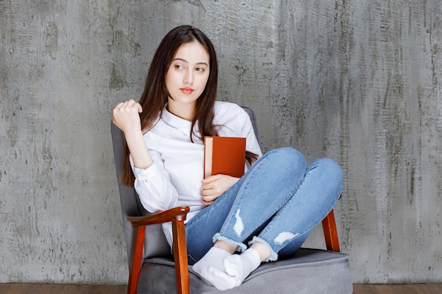 Portret van een vrouw zittend op een fauteuil met boek poseren. Hoge kwaliteit foto