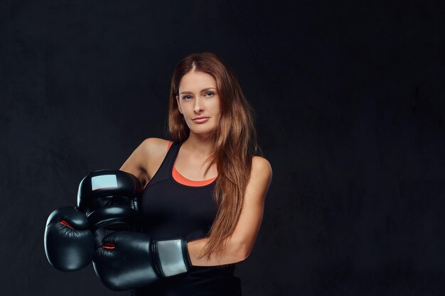 Portret van een vrouwelijke bokser die handschoenen draagt, houdt een beschermende helm vast die in een studio poseert. Geïsoleerd op een donkere gestructureerde achtergrond.