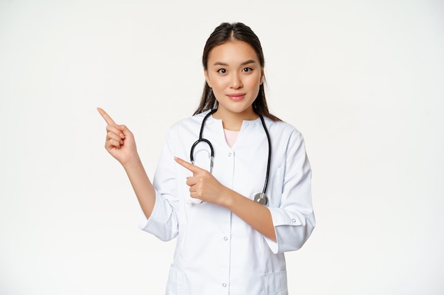 Portret van een vrouwelijke verpleegster in medisch uniform, wijzende vingers naar links, met ziekenhuisgerelateerde inhoud, medische informatie opzij, witte achtergrond
