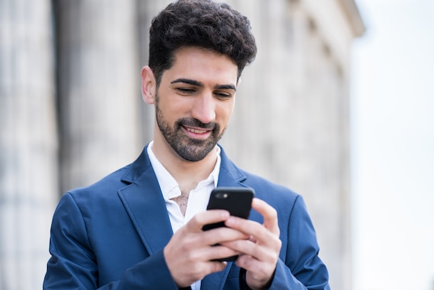 Portret van een zakenman die zijn mobiele telefoon gebruikt terwijl hij buiten op straat staat. Bedrijfs- en stedelijk concept.