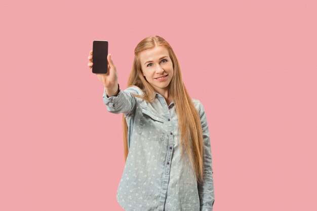 Portret van een zeker toevallig meisje die de lege scherm mobiele telefoon tonen die over roze muur wordt geïsoleerd