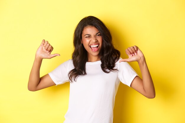 Portret van een zelfverzekerde en gelukkige Afro-Amerikaanse vrouw die met de vinger naar zichzelf wijst en trots lacht