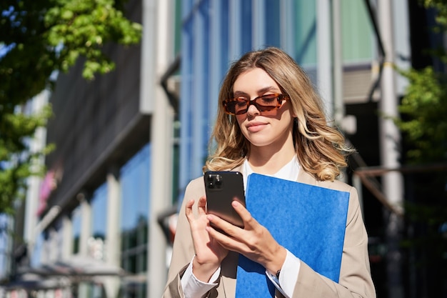 Portret van een zelfverzekerde zakenvrouw die op straat in de buurt van een kantoorgebouw staat met behulp van een mobiele telefoonbestelling