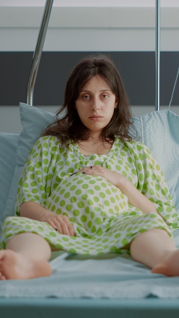 Portret van een zwangere persoon die in het ziekenhuisbed zit met een monitor die zich voorbereidt op de bevalling van het kind in de kliniek. Blanke jonge vrouw die zich ongeduldig voelt en weeën verwacht