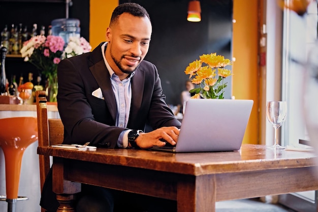 Portret van elegante zwarte man met behulp van een laptop in een restaurant.
