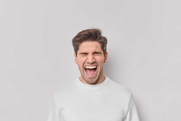 Portret van emotionele man schreeuwt van verbazing houdt mond wijd open schreeuwt luid draagt casual jumper geïsoleerd op witte achtergrond. Opgewonden mannelijk model reageert op geweldig nieuws of verrassing