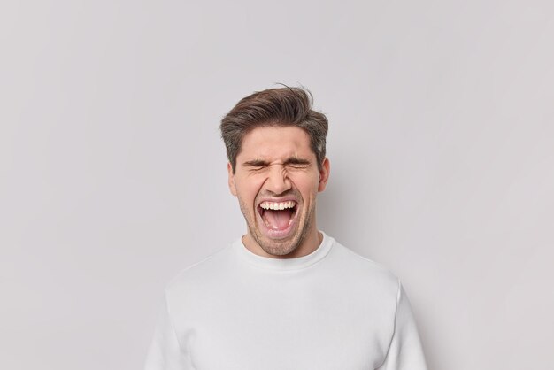 Portret van emotionele man schreeuwt van verbazing houdt mond wijd open schreeuwt luid draagt casual jumper geïsoleerd op witte achtergrond. Opgewonden mannelijk model reageert op geweldig nieuws of verrassing