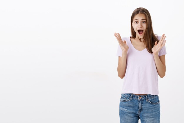 Portret van emotionele mooie jonge Europese vrouw in casual t-shirt schreeuwen van verbazing en vreugde verhogen en gebaren met palmen