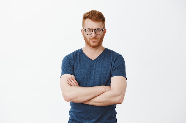 Portret van ernstig ogende knappe volwassen man met varkenshaar in koele glazen, staren, vingers kruisen op de borst