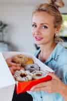 Gratis foto portret van europese vrouw met blonde haren genieten van donuts in keuken thuis villa.